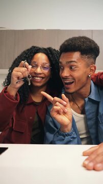 Vertical African american couple holding and showing the key to their new apartment or house to the camera. People being home owners or tenants of a property after signing a mortgage. Ownership