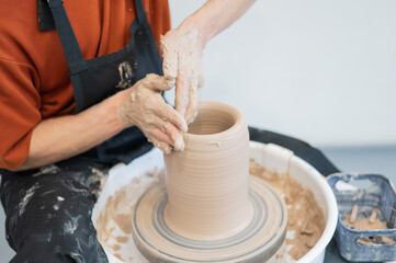 Close-up of a potter's hands making a ceramic vase on a potter's wheel. 