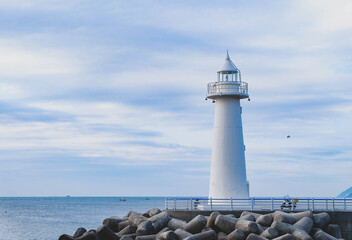 A small white lighthouse stands at the end of a breakwater