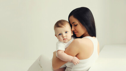 Happy young mother holding cute baby together in white room at home