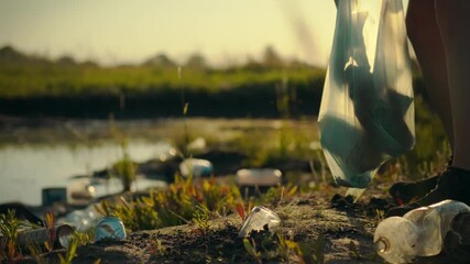 A man cleans the shore of a pond, collecting plastic garbage. He sorts plastic bottles and other waste into a trash bag for further recycling and maintaining a sustainable recycling process