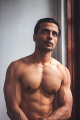 Fototapeta premium A fit Indian male with a lean physique, sitting in sadness, battles depression and a profound lack of self-confidence, his expression heavy with emotional struggle.