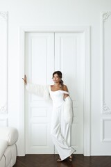 Stylish young woman with long dark hair models a white suit in a bright white room. Contemporary fashion shoot with minimalist aesthetics
