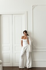 Beautiful brunette woman dressed in a sleek white suit poses gracefully in a bright, all-white photo studio. Stylish and professional image for business concepts