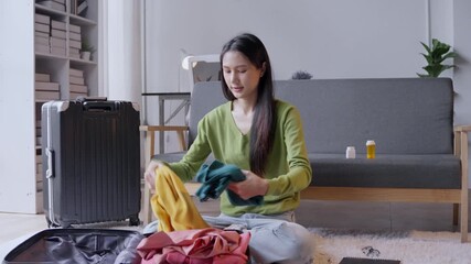 Woman carefully packs clothes into a suitcase, preparing for a trip. She organizes her colorful wardrobe in a modern living room, displaying neat packing skills