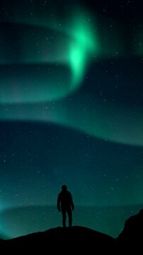 Aurora Borealis Green fluor Northern Lights and silhouette man watching. Winter landscape with polar weather in Arctic. Starry night sky scenery background 4k. Vertical, phone wallpaper
