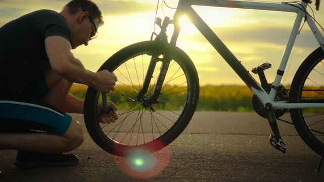 Sport. A young tourist outdoors uses a pump to inflate a tire on an asphalt road. General view of the camera, a young tourist maintains the wheels of a bicycle, maintains fitness, a tourist