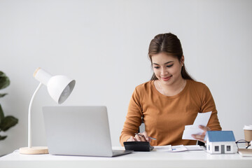 Young Woman Planning Finances for Buying a House, Using Calculator and Laptop at Home Office Desk