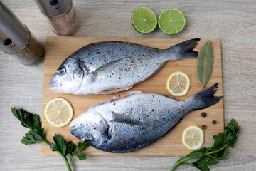 Two Fresh Fish on a Cutting Board with Spices and Herbs. Two whole, fresh fish are laid out on a...