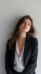 Fototapeta premium Stylish Young Woman in Black Blazer and White Shirt Leaning Against White Wall