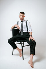 A man with white shirt and tie sits on a chair in studio. Barefoot