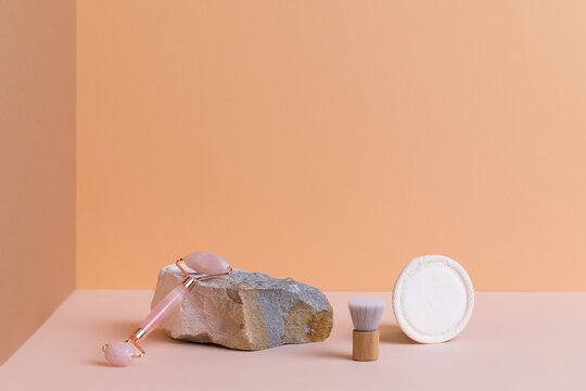 Gua sha facial roller and dry cosmetic brush resting on natural stone 