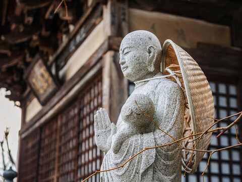 A stone statue of a monk standing near a traditional japanese temple