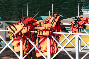 Several bright orange life jackets neatly hung on a white railing at a dock near a body of water