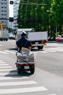 A man on a scooter in a city street carrying a stack of packages