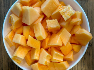 Fresh, cut up orange cantaloupe in a white bowl on a wooden table