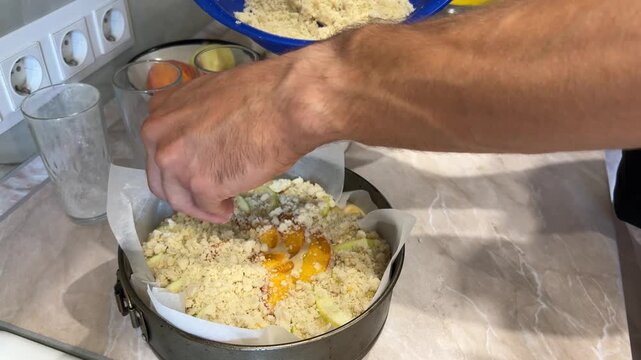 Chef's hands layer fresh peach slices and crumbly topping in a springform pan, preparing a delicious peach crumble dessert in a kitchen