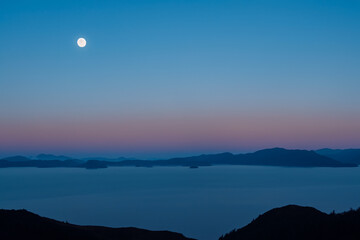 A full moon over mountains at sunset in nature. Mountain scenic sunrise concept. A full moon rises over the mountains at sunset in nature. A full moon rises over the mountains at sunset a against.