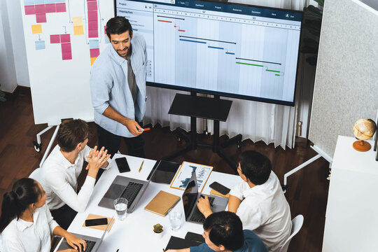Project manager communicate and collaborate with team using project management software display on monitor, tracking progress of project task and making schedule plan at meeting table. Prudent