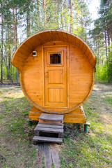 Round wooden sauna in the forest. Mobile sauna in the form of a barrel in the forest outdoors. Vertical photo