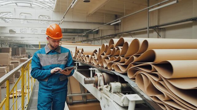 Worker controls quality of corrugated cardboard on a conveyor line for production of cardboard packaging. Paper factory, worker, recycling used paper into cardboard for packaging. Employee is working