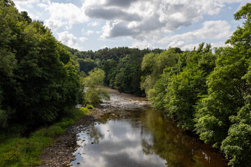 Fototapeta premium Photo of the beautiful town of Richmond which is a market town and civil parish in North Yorkshire, England showing the river with trees either side in the summer time
