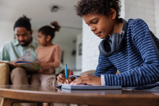 Boy doing homework while family in background