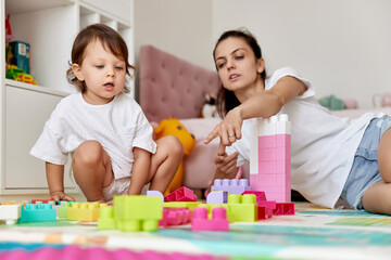 cute baby girl and her loving mother playing with toy bricks in the children room, early development