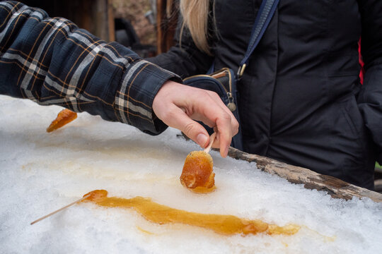 Hands rolling maple toffy on snow