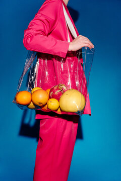 Person in pink suit carrying transparent bag of citrus fruits