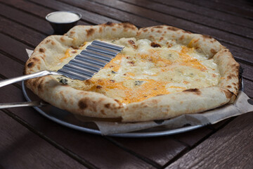 View of pizza with gorgonzola, cheddar, parmesan cheeses on a wooden table. Lifestyle background.
