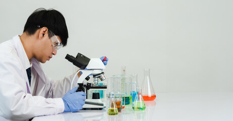 Fototapeta premium Portrait asian man student scientist Wearing a doctor gown in the lab looking hand at chemist. caused by mixing reagents in scientific research laboratories with test tubes and microscope on the table