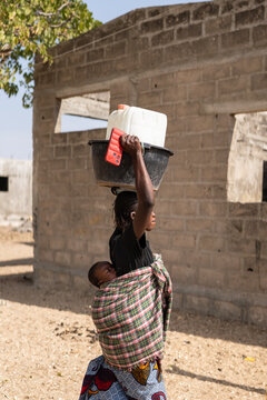 Mother carrying baby and water on her head in senegal, africa
