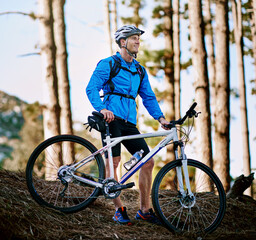 Obraz premium Man, thinking and happy or bike in woods for adventure and transport for outdoor journey. Cyclist, helmet and ideas or smile for fitness, wellness or trees in forest or nature for exercise and health