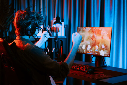 Host channel of young gaming streamer getting to win fighting Moba at battle arena with multiplays team, wearing headphone on pc monitor with back side image at neon digital light modern room. Gusher.