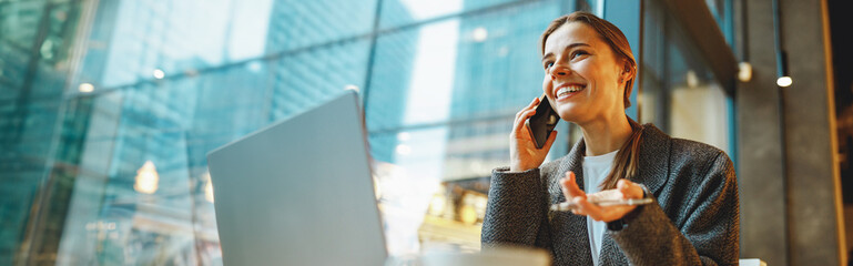 Young female freelancer talking with client and work on laptop in cafe. Distance work concept