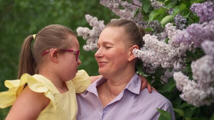 Amidst blooming lilacs, mother and her young daughter with Down syndrome share tender kiss and embrace. Girl is wearing yellow dress, and moment reflects love and support children with special needs