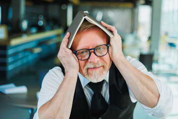 Emotional old man in glasses with a notebook in the office. An old businessman grimaces on his forehead.