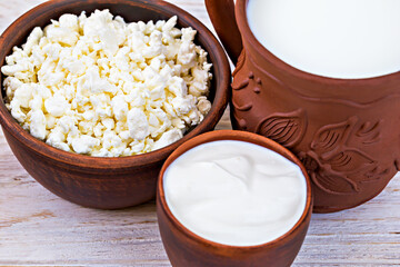 Close up of traditional dairy products including cottage cheese, sour cream and milk in decorative clay bowls on rustic wooden table. Ideal for food presentations and healthy eating concepts