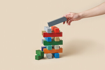 Hand placing grey container on tower build in perpendicular way