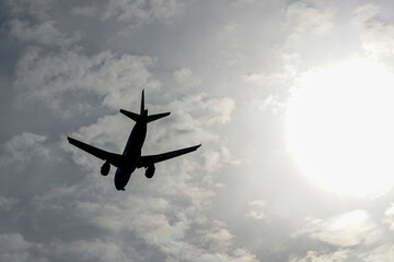 Black silhouette of a large plane against the background of gray clouds and bright sunlight