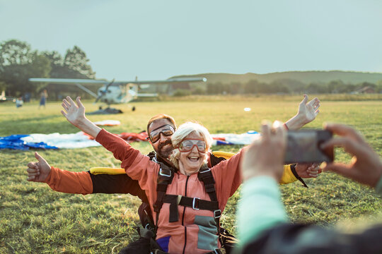 Elderly woman tandem skydiving with instructor, celebrating landing