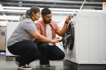 Happy young indian couple buying washing machine in appliances store