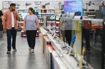 Beautiful couple buying consumer tech products in modern home appliances store. They are choosing home theater and TV devices