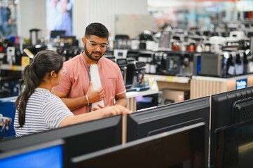 Beautiful couple buying consumer tech products in modern home appliances store. They are choosing home theater and TV devices