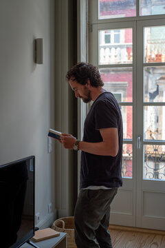 Man checking a book standing by a tv at home