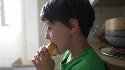 Profile close-up face of young boy eating piece of bread. Child snacking food