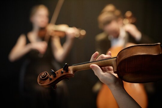 Close up on hand of unrecognizable female string ensemble musician playing on violin moving fingers on fretboard on blurred background, focus on hand, copy space