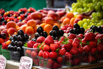 Close up of bowls of fresh and delicious strawberries and plums sold at a local market.