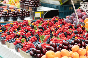 Market stall displaying a variety of red fruits, including strawberries, blueberries, blackberries, plums, and others. Colorful image of fresh fruits in a local market.